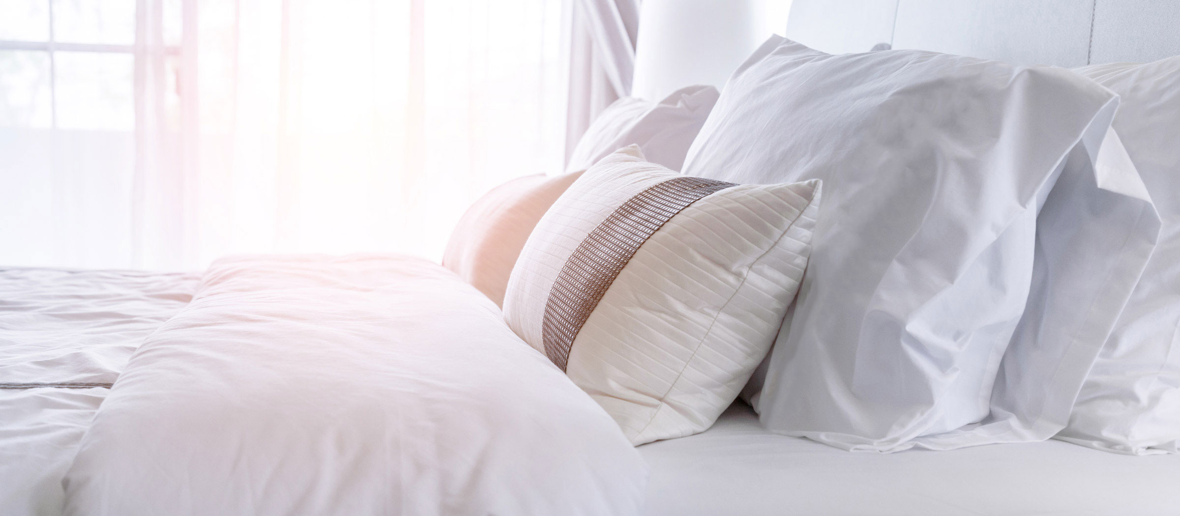 Warm morning sunlight shines over a freshly-made bed