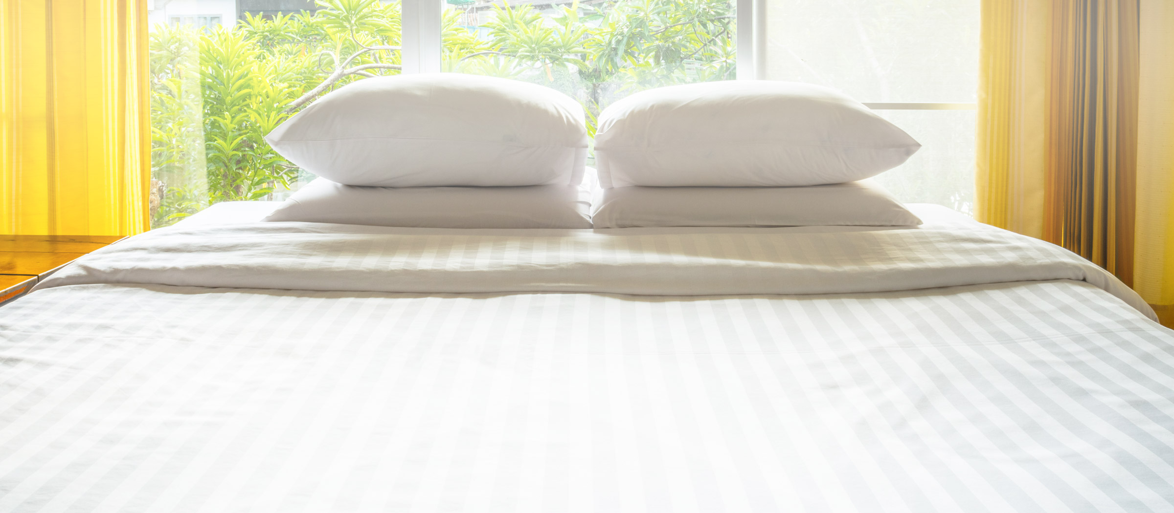 Clean bedsheets and pillows before an outdoors-facing window
